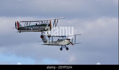 Vintage De Havilland 1928 DH60X Moth Doppeldecker und Avro 621 Tutor Doppeldecker Flugzeuge im Flug wolkigen Himmel. Stockfoto