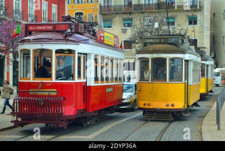 Drei traditionelle rote und gelbe Lissabonner Straßenbahnen auf Largo das Portas do Sol blockieren den Verkehr. Stockfoto