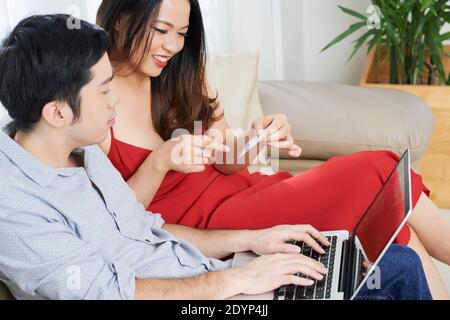 Junge lächelnde vietnamesische Paar mit Kreditkarte Online-Shopping zusammen Über Laptop Stockfoto