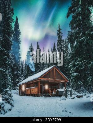 Aurora Borealis über Holzhütte mit Rauch auf Schnee im Pinienwald im Yoho Nationalpark, Kanada Stockfoto