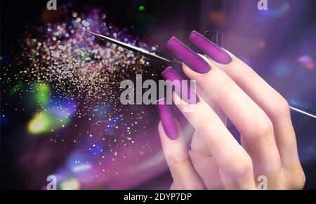 Hand mit einer schönen Maniküre und einem Pinsel auf einem lila Bokeh Hintergrund. Nagellack. Verlängerte Nägel. Stockfoto