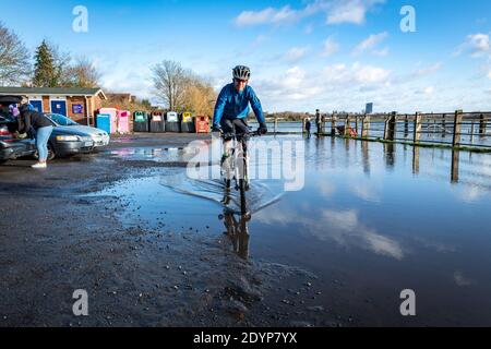 Wolvercote, Oxfordshire, Großbritannien. 27. Dezember 2020. Der Einwohner von Oxford Stephen Charters radelt durch den überfluteten Parkplatz. Überschwemmungen in Oxfordshire. Sturm Bella brachte noch mehr Regen nach Oxfordshire und verursachte Überschwemmungen in tief liegenden Gebieten. Viele Menschen sind aus der Ausübung in der Sonne. Kredit: Sidney Bruere/Alamy Live Nachrichten Stockfoto