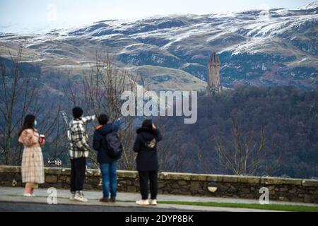 Stirling, Schottland, Großbritannien. Dezember 2020. Im Bild: Tag zwei der festlichen Phase 4-Sperre für das schottische Festland. Eine kleine Gruppe chinesischer Touristen, die Gesichtsmasken tragen, schaut auf das Wallace Monument vom Aussichtspunkt des Stirling Castle, das einen Blick auf Meilen herum bietet. Ein kleines Fenster im Wetter taucht aus der gelben Wetterwarnung auf, die ausgegeben wurde, als Storm Bella über Nacht Schneefall gibt und einen Staubwedel von Weiß auf den Ochill Hills hinterlässt. Quelle: Colin Fisher/Alamy Live News Stockfoto