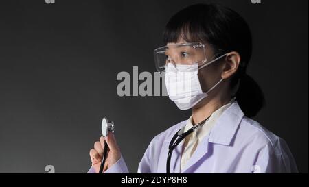 Arzt trägt medizinische Maske und klare Brille oder Brille und Stethoskop am Hals und weiße Uniform. Asiatische Ärztin oder Wissenschaftlerin im Schutz Stockfoto