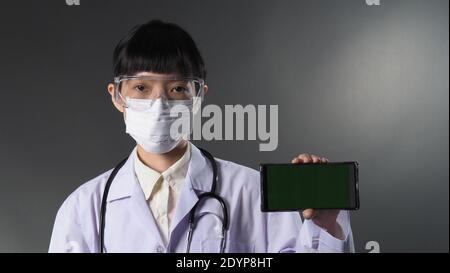 Arzt trägt medizinische Maske und klare Brille oder Brille und Stethoskop am Hals und weiße Uniform. Asiatische Ärztin oder Wissenschaftlerin im Schutz Stockfoto