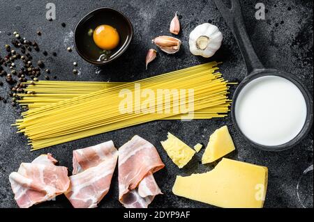 Zutaten für traditionelle italienische Pasta alla Carbonara. Ungekochte Spaghetti, Pancetta Speck, Parmesan Käse, Ei. Schwarzer Hintergrund. Draufsicht Stockfoto