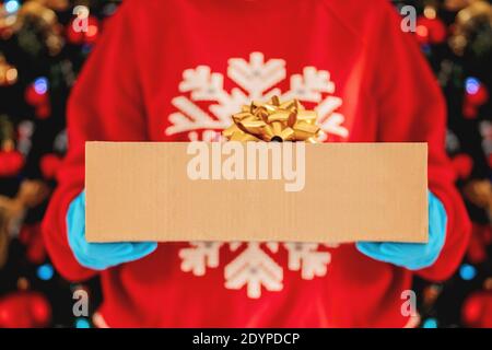 Delivery Mann hält Pappkartons, Geschenk in medizinischen Gummihandschuhen auf dem Hintergrund eines Weihnachtsbaums. Express-Lieferung. Stockfoto
