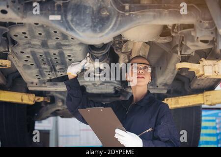 Weibliche Mechanikerin, die ein angehobener Wagen inspiziert Stockfoto