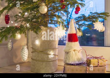 Weihnachtslaterne, Weihnachtsknome, Weihnachtsbaum und rotes Dekor auf dem Fenster eines Holzhauses mit Blick auf den Wintergarten. Stockfoto