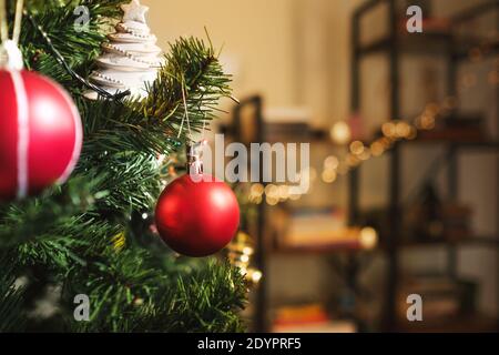 Weihnachtsschmuck, der an einem Zweig eines weihnachtsbaums in einem Raum mit einem entkokchten Bücherregal auf dem Hintergrund hängt. Stockfoto