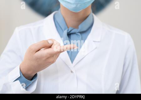 Hand der jungen zeitgenössischen Augenärztin in Whitecoat und Schutz Maske mit Kontaktlinse am Zeigefinger vor der Kamera Stockfoto