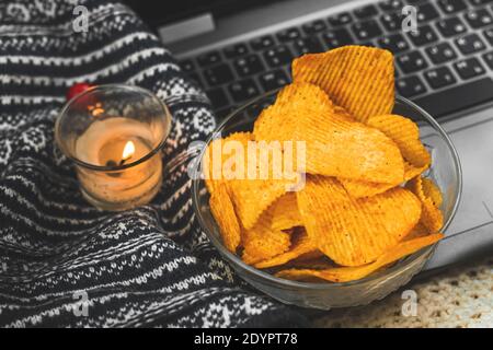 Gemütliche Winter- und Herbstabende mit Filmuhr und ungesunden Speisen, Kartoffelchips in Schale, Strickpullover aus nächster Nähe Stockfoto