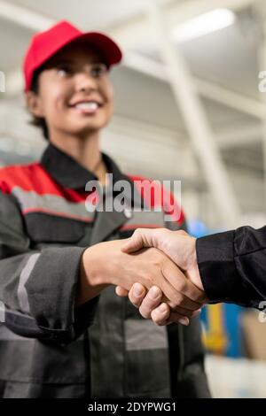 Hand der jungen erfolgreichen weiblichen Ingenieurin in Arbeitskleidung Gruß Kollegin Oder Vorarbeiter durch Handschlag gegen riesige technische Konstruktion Stockfoto
