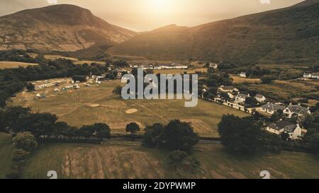 Sonnenuntergang Antenne am Dorf Berg . Niemand Naturlandschaft bei Sonnenuntergang. Hütten, Häuser an der Straße. Whiskey Destillerie im Tal. Cinematic Loch-Ranza, Arran Island, Schottland, Vereinigtes Königreich, Europa Stockfoto