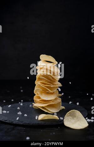 Kartoffelchips und Salz in der Zusammensetzung auf schwarzem Hintergrund. Stockfoto