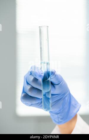 Handgebliebene Hand von zeitgenössischen jungen Forscher hält Flasche mit reinem Wasser vor der Kamera während des wissenschaftlichen Experiments im Labor Stockfoto