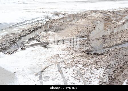 Nahaufnahme einer Schuttstraße mit Schlaglöchern, großen schlammigen Pfützen und geschmolzenem Schnee. Hochwertige Fotos Stockfoto