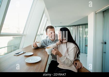 Junges Paar flirtet im Café. Schöne Frau mit langen dunklen Haaren und gut aussehenden Mann mit stilvollen Haarschnitt Blick auf einander, halten Kaffee Stockfoto