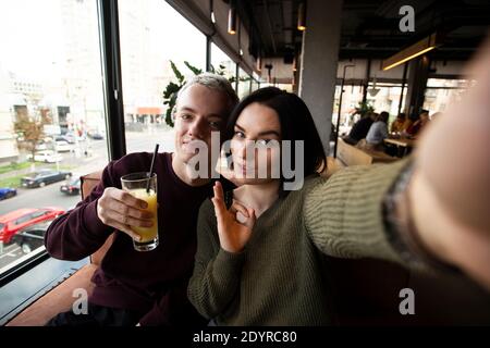 Junges Paar posiert für Selfie in öffentlichen Ort. Attraktive Brünette Frau und gut aussehende blonde Mann Foto in einem Restaurant zusammen. Der Mensch hält einen Stockfoto