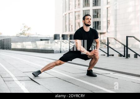 Läufer macht seitliche Ausfallschritte. Portrait eines sportlichen Mannes, der vor dem Training Dehnübungen macht. Männlicher Sportler, der sich für das Joggen im Freien vorbereitet. Sport aktiv Stockfoto