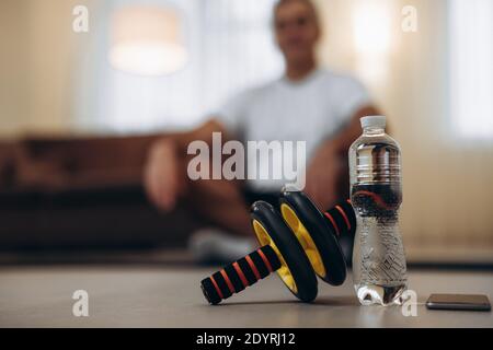 Kümmern Sie sich um Ihren Körper Nahaufnahme Sportgeräte. Übungsrad. Wasserflasche aus Kunststoff. Verschwommener Mann in der bequemen Sitzposition sitzend mit kreuzenden Beinen Stockfoto