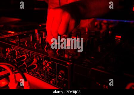 DJ-Mixer in hellrotem Licht. Nahaufnahme von männlichen Hand drehenden Tumblern auf der DISK-Jockey-Konsole schneiden. Nightlife-Konzept. Rave auf der Party mit gut Stockfoto