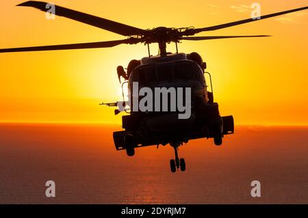 Eine Luft-Luft-Ansicht eines Naval Sikorsky S70B Seahawk Hubschraubers in Silhouette, bei Sonnenuntergang. Stockfoto