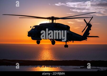 Eine Luft-Luft-Ansicht eines Naval Sikorsky S70B Seahawk Hubschraubers in Silhouette, bei Sonnenuntergang. Stockfoto