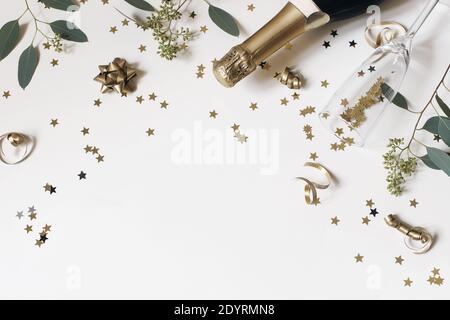 Frohes neues Jahr Stillleben. Leeres Sektglas, Weinflasche mit goldenen Konfetti-Sternen und Eukalyptuszweigen isoliert auf weißem Tischhintergrund, c Stockfoto