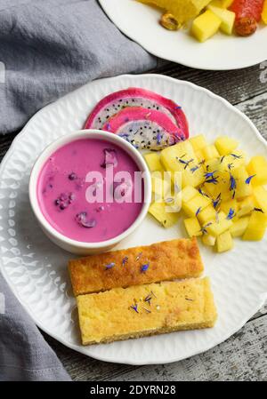 Mangobrot mit Joghurt auf pflanzlicher Basis und frischen Früchten, leuchtende Farben, bunte Mahlzeit, flaches Lay Stockfoto