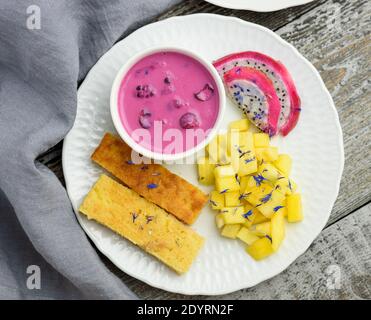 Mangobrot mit Joghurt auf pflanzlicher Basis und frischen Früchten, leuchtende Farben, bunte Mahlzeit, flaches Lay Stockfoto