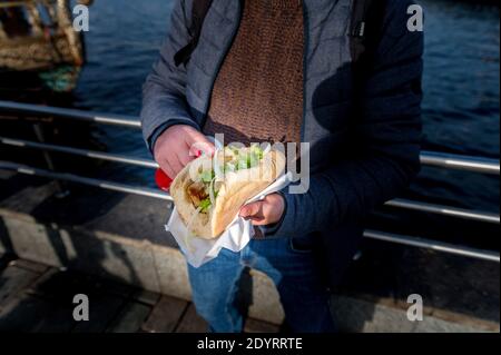 Mann hält Sandwich mit gegrilltem Fisch in Istanbul. Essen auf der Straße ist ein Teil des lokalen Lebens in hier. Gesundes Fast-Food-Konzept. Selektiver Fokus. Stockfoto