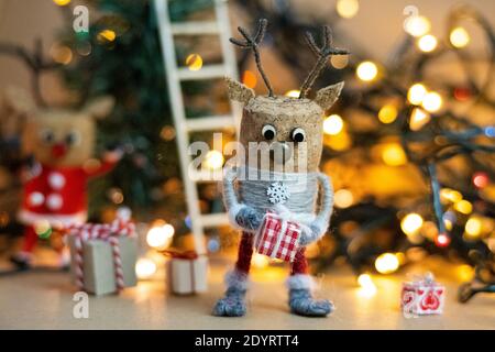 Weinkorken-Rentiere feiern Weihnachten Eröffnung ein kleines Geschenk vor warmen, weihnachtlichen Lichtern im Hintergrund. Stockfoto