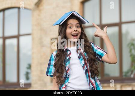 Lesen zu ihrem eigenen Vergnügen. Happy Child Point in der Bibliothek Buch auf Kopf. Schulbibliothek. Niedlicher Bücherwurm. Schulbildung. Wissenstag. Bibliopole. Buchhandlung. Tief in die Entwicklung der Alphabetisierung. Stockfoto