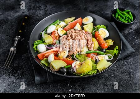 Thunfischsalat mit Gemüse, Eiern und Sardellen auf einem Teller. Schwarzer Hintergrund. Draufsicht Stockfoto
