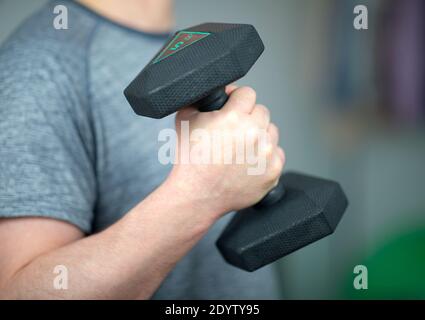 Training mit Hanteln zu Hause. Ein Mann trainiert zu Hause mit Hanteln. Hand am Ellbogen gebeugt, die Hantel haltend Stockfoto