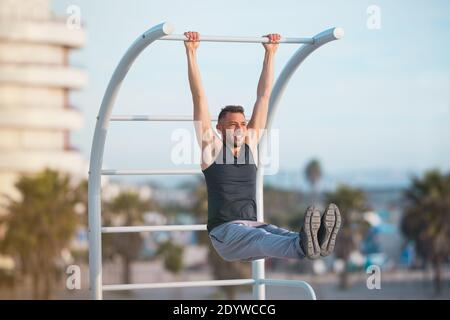 Fit Mann Ausübung seiner bauchmuskeln mit hängenden Bein hebt. Mann macht Pull-ups im Freien Stockfoto