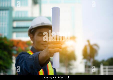 Engineering Holding Plan und trägt einen weißen Schutzhelm während der Arbeit. Hintergrundstruktur des Gebäudes Stockfoto