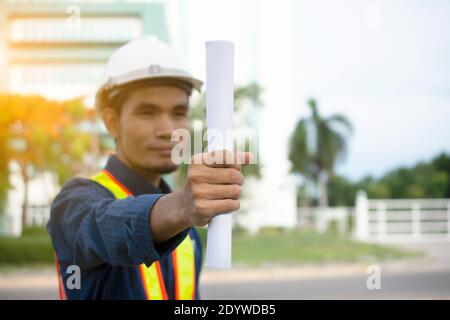 Engineering Holding Plan und trägt einen weißen Schutzhelm während der Arbeit. Hintergrundstruktur des Gebäudes Stockfoto