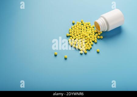 Gelbe Vitamin C Kapseln verschüttet aus einem weißen Glas vor einem blauen Hintergrund. Achten Sie auf Ihre Gesundheit. Vitamine und Mineralstoffe. Freier Speicherplatz Stockfoto