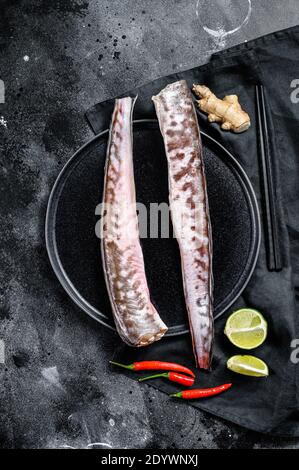 Roher King-Lip, Congrio-Fisch mit Zutaten zum Kochen, Limette, Ingwer-Chili-Pfeffer. Schwarzer Hintergrund. Draufsicht Stockfoto