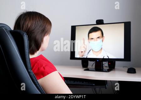 Online-Beratung mit einem Arzt, Frau hört sich die Arztempfehlungen sitzen vor der PC-Webcam. Mann in medizinischer Maske auf dem Display Stockfoto