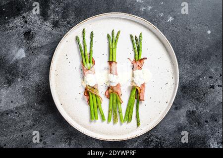 Gegrillter Bio-Spargel in Schweinebackschinken eingewickelt. Schwarzer Hintergrund. Draufsicht Stockfoto