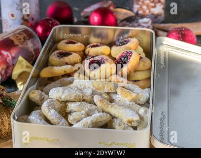 Eine Schachtel mit weihnachtskeksen auf einem Küchentisch mit Weihnachtsdekoration. Winkels Augen mit Marmelade Füllung und deutsch Vanillekipferl Stockfoto