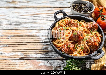 Italienische Pasta-Spaghetti mit Tomatensauce und Fleischbällchen in gusseiserner Pfanne mit Parmesan. Weißer Holzhintergrund. Draufsicht. Speicherplatz kopieren Stockfoto