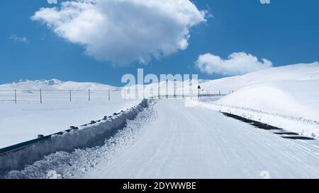 Biegen Sie die Straße mit Schnee und weißen Wolken am blauen Himmel in Tibet, westlich von China ab. Stockfoto