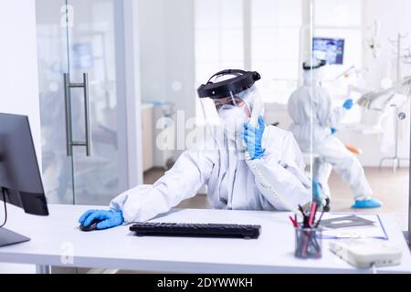 Zahnarzt Krankenschwester in psa in Stomatologie Klinik während covid-19 Gespräch mit dem Patienten über Telefon gekleidet. Medizin-Team trägt Schutzausrüstung gegen Coronavirus Pandemie in der Zahnaufnahme als Sicherheitsmaßnahme. Stockfoto