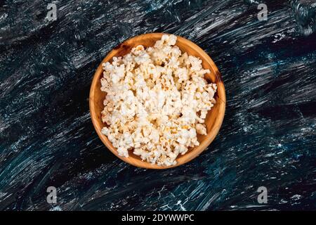 Popcorn in runder Holzschale auf schwarzem Texturhintergrund, Movie Night Snack. Copyspace Stockfoto