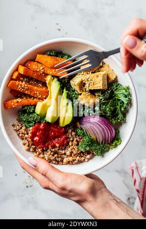 Gebackenes Gemüse, Avocado, Tofu und Buchweizen buddha Schüssel. Veganer Lunch-Salat mit Grünkohl, gebackenen Süßkartoffeln, Tofu, Buchweizen und Avocado in einer weißen Schleife Stockfoto