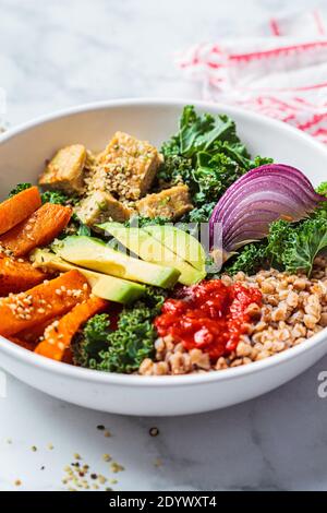 Gebackenes Gemüse, Avocado, Tofu und Buchweizen buddha Schüssel. Veganer Lunch-Salat mit Grünkohl, gebackenen Süßkartoffeln, Tofu, Buchweizen und Avocado in einer weißen Schleife Stockfoto